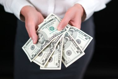 Beş dolarlık banknotlar, iş elbiseli, beyaz gömlekli ve gri etekli, siyah arka planda bir kadının elinde. Kar, para, finans, tasarruf, yatırım, mali istihbarat kavramı.