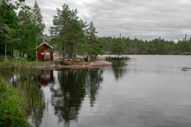 Skuleskogen, İsveç - 08.22.2021: Bulutlu bir günde İsveç 'teki Skuleskogen Ulusal Parkı' nda deniz kıyısında kırmızı ahşap kulübe
