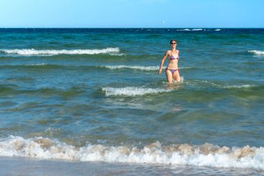 Attractive sporty short haired woman in her thirties, wearing bikini, standing in the blue sea with her arms spread on a sunny summer day. Concept for holiday, vacation, relaxation, mental health,joy