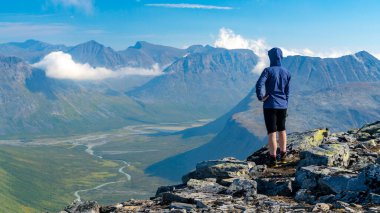 Dağın tepesinden geniş arktik dağ manzarasına bakan mavi ceketli kadın yürüyüşçü. Naite Tepesi, Sarek Ulusal Parkı, İsveç. Laponya 'da yürüyüş. Kuzey Kutbu 'nda açık hava macerası