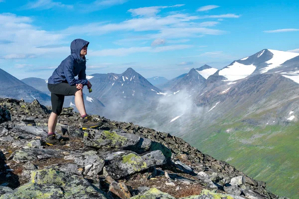 Dağın tepesinden geniş arktik dağ manzarasına bakan mavi ceketli kadın yürüyüşçü. Naite Tepesi, Sarek Ulusal Parkı, İsveç. Laponya 'da yürüyüş. Kuzey Kutbu 'nda açık hava macerası
