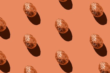 Easter eggs pattern in aluminum foil on coral background.Easter holiday creative concept. Sharp shadows, flatlay.