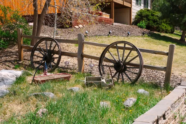 Gård, trädgård eller trädgård på landet dekoration med gamla trä vagn hjul, liten leksak vagn, växt kruka och amerikansk flagga i gräs med dekorativa stenar på staketet foto — Stockfoto