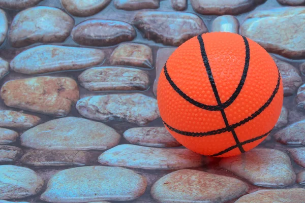 Basketball ball on pebbles cobblestone road surface close up background photo texture with copy space. Orange rubber ball toy.