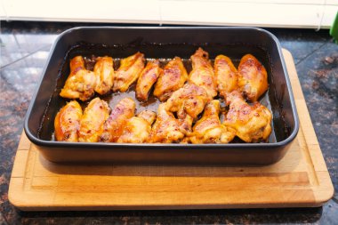 Yeni pişmiş tavuk kanatları ahşap kesme tahtasının üstünde mutfak tezgahı yüzeyinde üst manzara yemek fotoğrafını yakın. Fırından çıkmış ev yapımı ızgara tavuk. Evde yemek pişirmek..