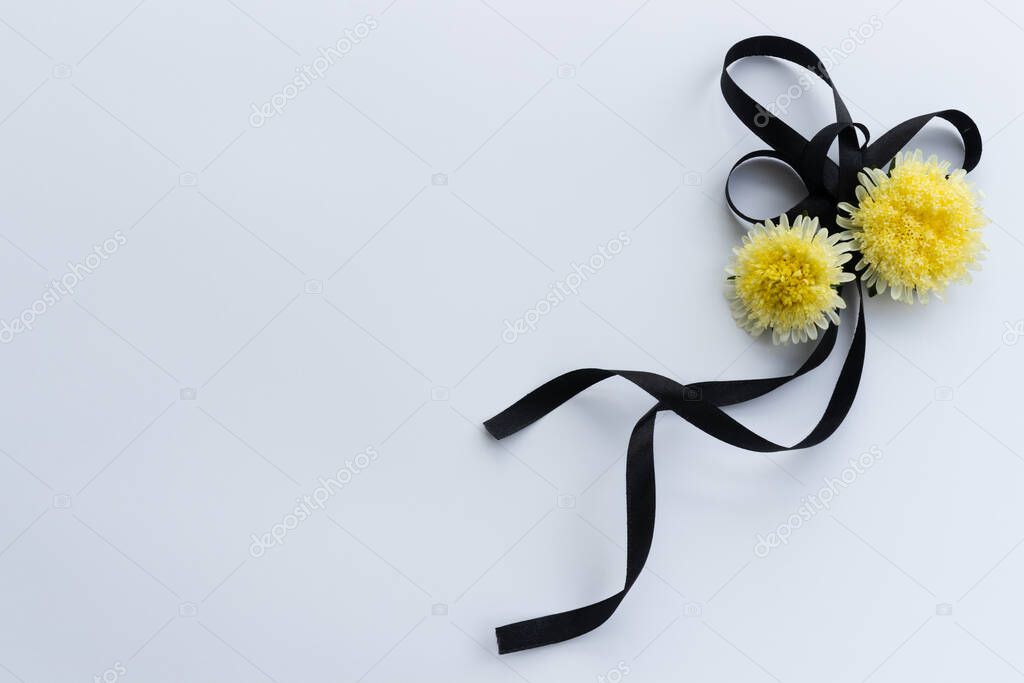 Black funeral ribbon with two yellow flowers.