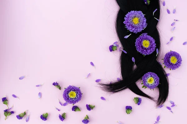 Pigtail de cabelo escuro com flores lilás frescas nele. Conceito de cuidados capilares. — Fotografia de Stock