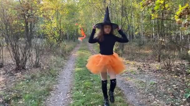 Kleine Hexe mit Zauberstab tritt auf einen Waldweg. Halloween-Konzept. — Stockvideo