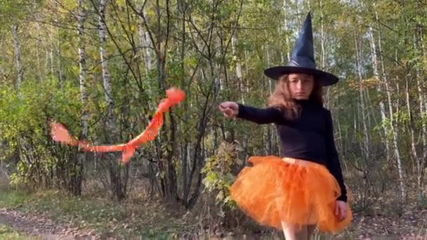 4K Niña bruja con varita mágica se encuentra en un sendero forestal. Pequeña bruja linda. — Vídeo de stock