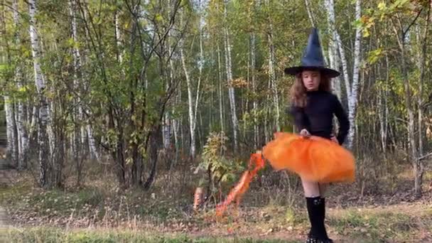 Petite fille sorcière avec baguette magique se tient sur un chemin forestier. Concept Halloween. — Video