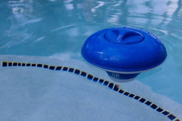 Dispensador de cloro plástico azul flotando en la superficie de una piscina. —  Fotos de Stock