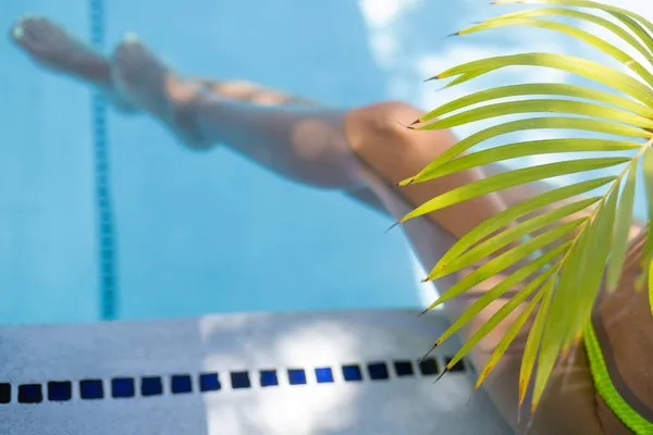 带棕榈叶的游泳池中的雌性腿。有选择的重点. — 图库照片