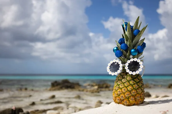 海滩上站着戴着印有圣诞球的太阳镜的菠萝. — 图库照片