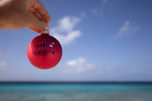 Main féminine tenant boule de Noël rouge sur le fond du paysage marin. — Photo