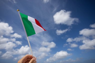 Rüzgarda dalgalanan İtalyan bayrağı. Mavi gökyüzünde, arka planda bulutlar olan kadın eli..