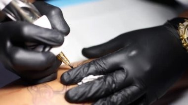 Dövme makinesi kapanıyor. Dövmecinin elleri deriye çizgi çiziyor. Seçici odak.