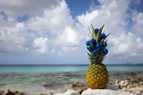 Ananas ozdobiony świątecznymi kulkami stoi na plaży. — Zdjęcie stockowe