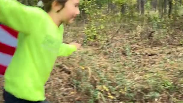 Petite fille qui court avec le drapeau américain sur un sentier forestier. Gros plan. — Video