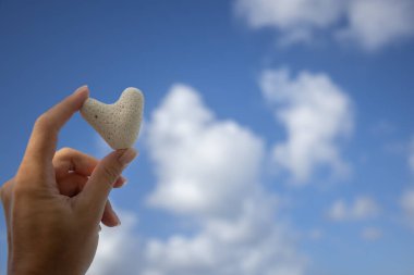 Deniz manzarasının arka planında mercandan küçük bir kalp tutan kadın el..