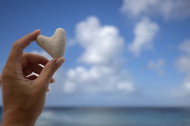 Deniz manzarasının arka planında mercandan küçük bir kalp tutan kadın el..