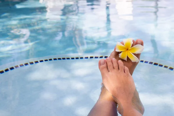在游泳池里的水里长有热带花的雌性脚。假日、美容美发、足部护理概念. — 图库照片