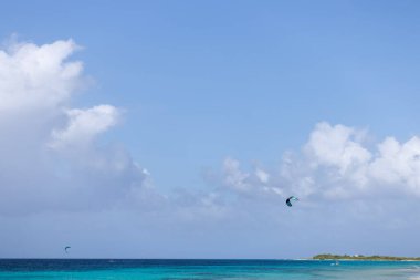 Uçurtmayı destekleyen dengeleyici paraşüt mavi gökyüzünde turkuaz denizin üzerinde uçuyor.