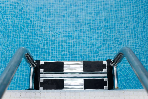 Barandillas de acero escaleras en una piscina con agua azul —  Fotos de Stock