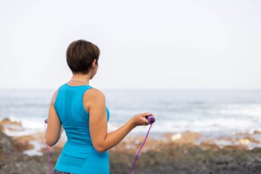 Denize yakın duran ip atlayan genç bir kadın. Dışarıda spor yapıyor..