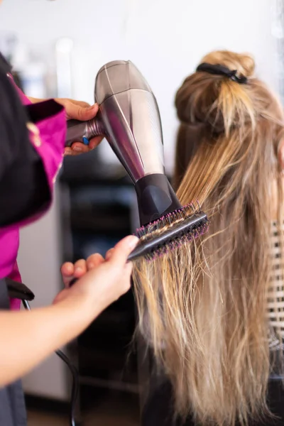 Asciugatura di capelli biondi con asciugacapelli e spazzola rotonda a parrucchiere. — Foto Stock