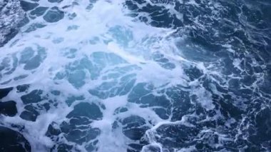 Sörf dalgalarının yukarıdan aşağıya doğru kayalıkların üzerinden beyaz su ile yuvarlanışını gösteren hava görüntüleri. 4k görüntü