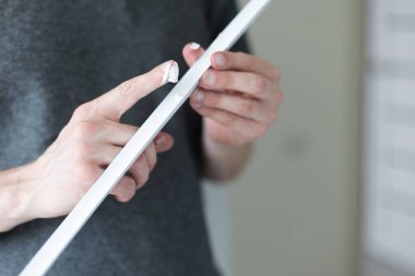 Adam apartmandaki duvar koruması için dekoratif plastik köşeye parmak yapıştırıcı sürüyor. Yakın çekim..