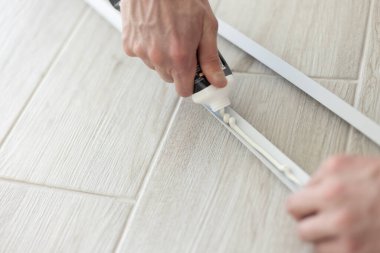 Mans hands putting glue out of tube to plastic construction detail