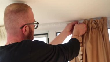 Merdivendeki adam perdeleri kaldırıyor. Yan görüş. Ev dekoru. 4K görüntü.