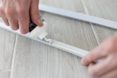 Mans elleri plastik inşaat detaylarına yapıştırıcıyı tüpten çıkarıyor. Yakın çekim.