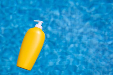Yellow sunscreen bottle floating in blue water of swimming pool.