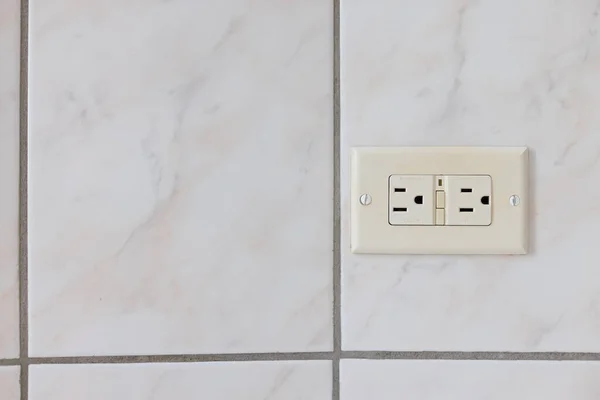 Electrical plug type B on the tiled wall in a bathroom