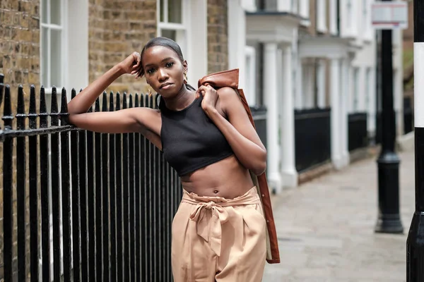 Deri ceketle poz veren siyah kadın portresi. Çitlere yaslanıyor..