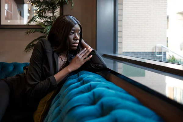 Elegante Zwarte Jonge Vrouw Kijkt Weg Zittend Een Bank Binnen — Stockfoto
