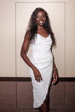 Beyaz elbiseli kameraya bakan gülümseyen siyahi genç kadın. Bir otelde kalıyor..