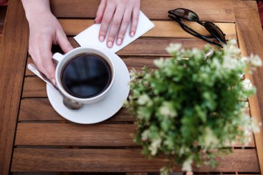 Bir fincan kahve içerken ellerinizi yakın tutun. Bir bitki, gözlük ve peçete var.. 