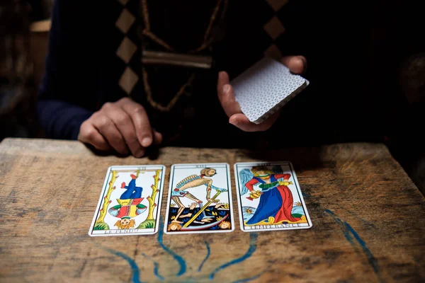 Ahşap masadaki psişik okuyucu kartlarını kapat. Üç tarot kartı ve okuyucunun elini görebiliyoruz..