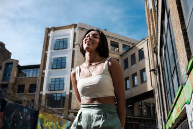 Shoreditch London 'da bir sokakta poz veren Asyalı genç bir model. Beyaz kolsuz bir tişört giyerek gülümsüyor..