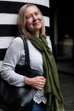 Çekici, olgun bir kadın Londra 'nın bir caddesinde kameraya bakıyor. O bir el çantası ve yeşil bir eşarp takıyor..