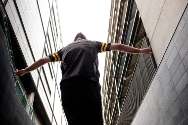 Man dancer performing between two modern buildings. He is wearing black casual outfit.