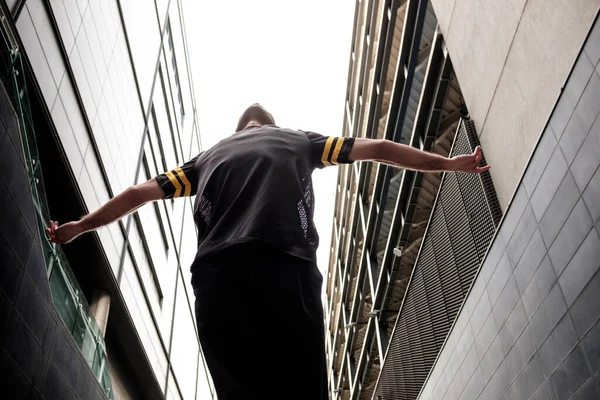 Man dancer performing between two modern buildings. He is wearing black casual outfit.