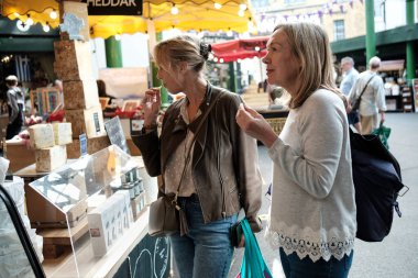 Two senior women friends enjoying shopping cheese in a street market. Borough market, London.
