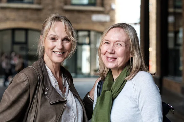 Two attractive mature women posing in a nature portrait in a street in London. They are smiling and looking at camera.