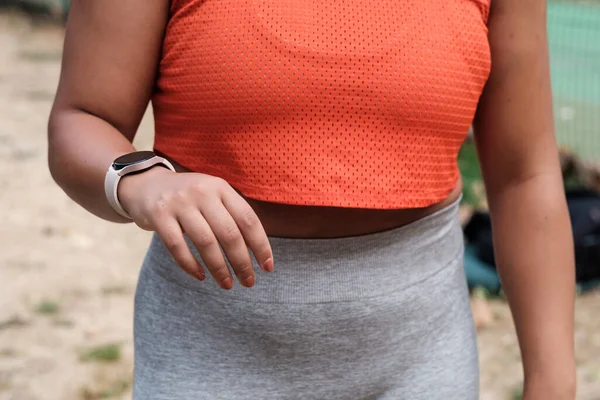 Close up of the hand of a curvy model wearing a sport watch. She is wearing leggings and orange sleeveless t-shirt.