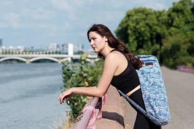 Young caucasian woman is wearing a mat yoga and she is looking at River Thames. Yoga and spirituality.