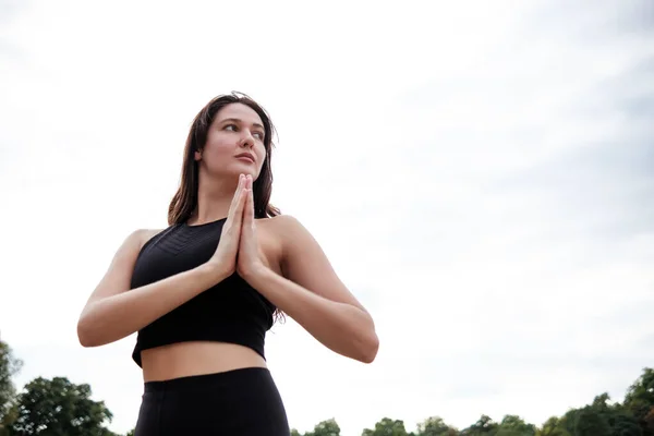 Portrait of spiritual caucasian woman doing yoga in a London Park. She is wearing a black yoga outfit. Healthy lifestyle concept.